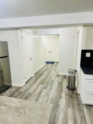 A kitchen with white cabinets, a stainless steel refrigerator, and a trash can.