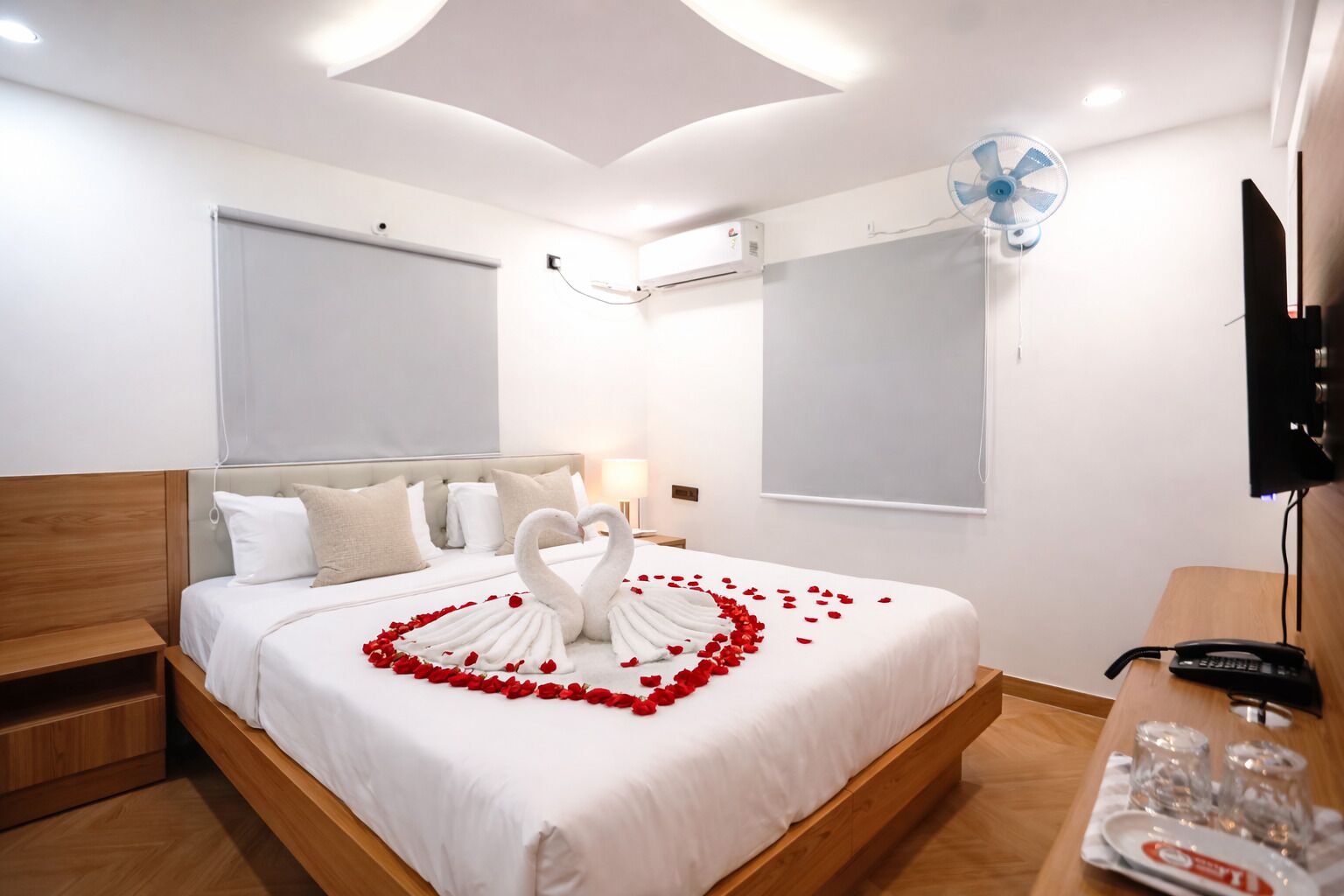 A hotel room with a bed, a desk, a TV, and a ceiling fan.