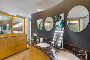 Une salle de bain moderne avec deux vasques, un meuble-lavabo avec des tiroirs, un grand miroir avec éclairage intégré et des éléments décoratifs muraux.