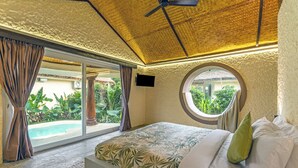 Un dormitorio con una cama grande, un ventilador de techo, un ventanal redondo y vistas a una piscina.