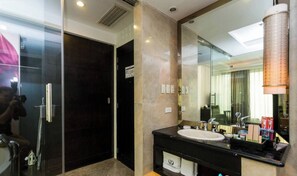 A modern bathroom with a glass shower enclosure, a dark door, a marble wall, a sink with a mirror, and a towel rack.