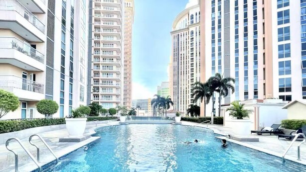 A swimming pool with clear water, surrounded by high-rise buildings, and equipped with poolside chairs and sun loungers. - AdahkuMaya Luxury Suites Plus (Taguig)