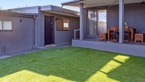 Une maison moderne dotée d’un patio couvert, d’une petite pelouse et d’un coin repas avec des meubles en bois.