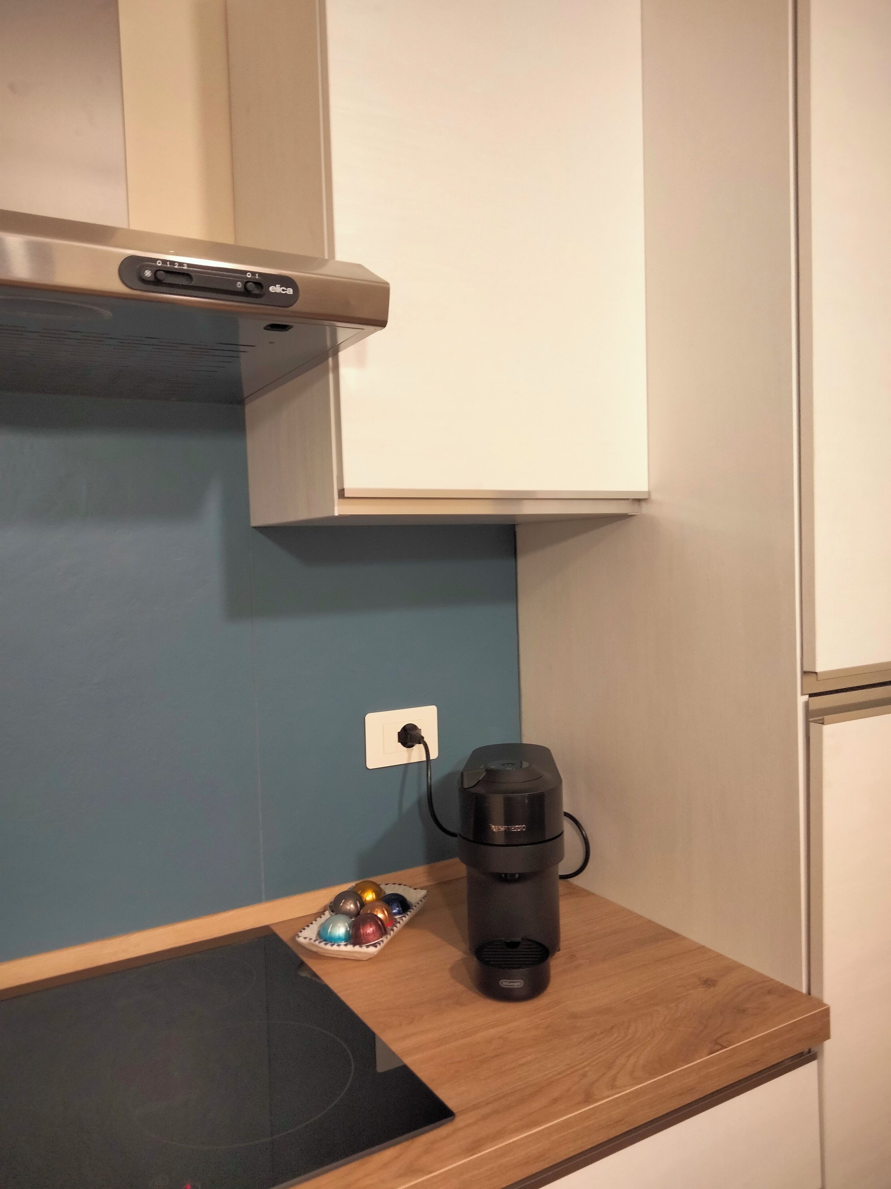 Une cuisine avec une machine à café sur le plan de travail, une tablette et une prise électrique.