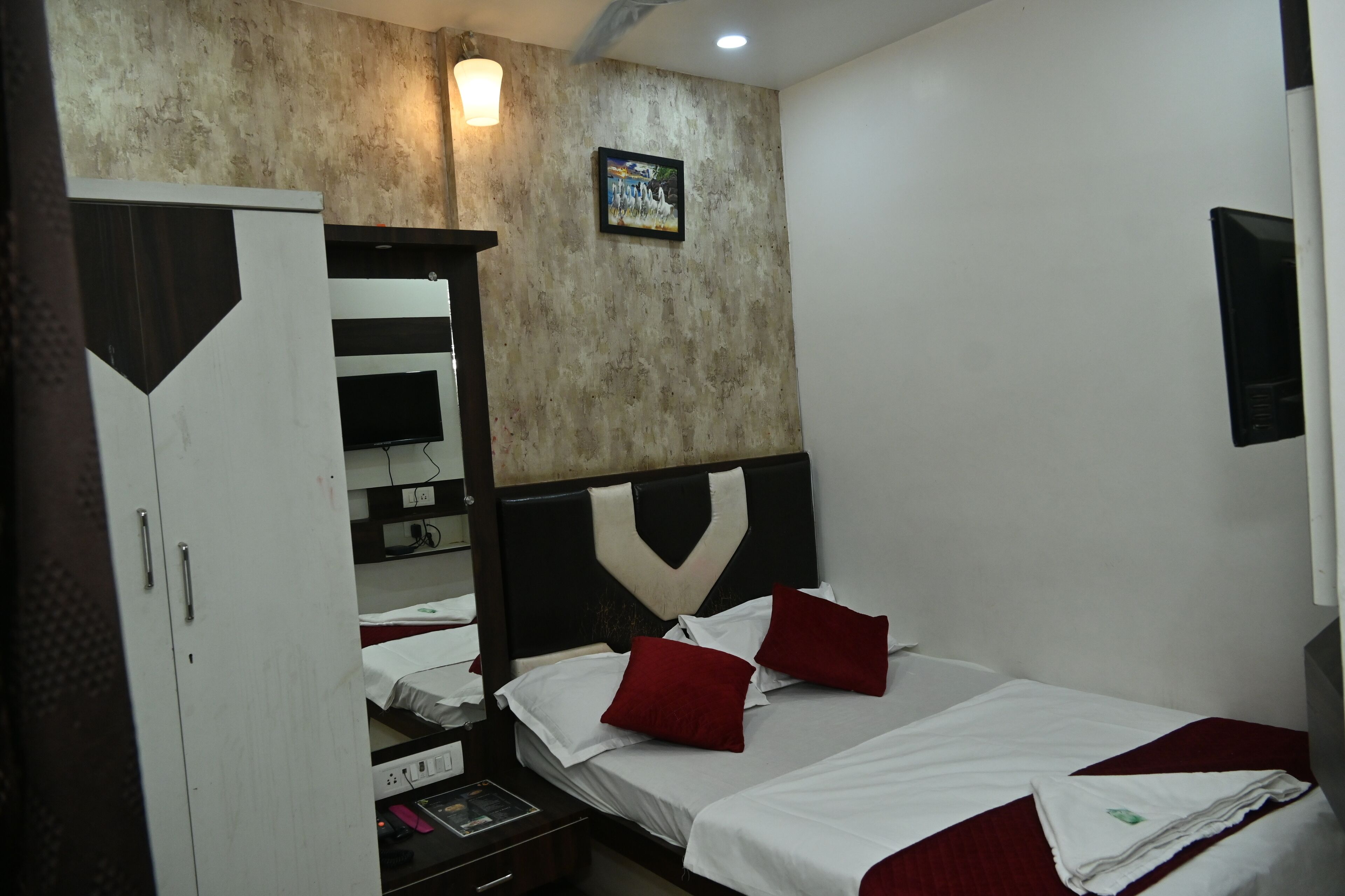 A hotel room with a bed, a wardrobe, a desk, and a wall-mounted TV.
