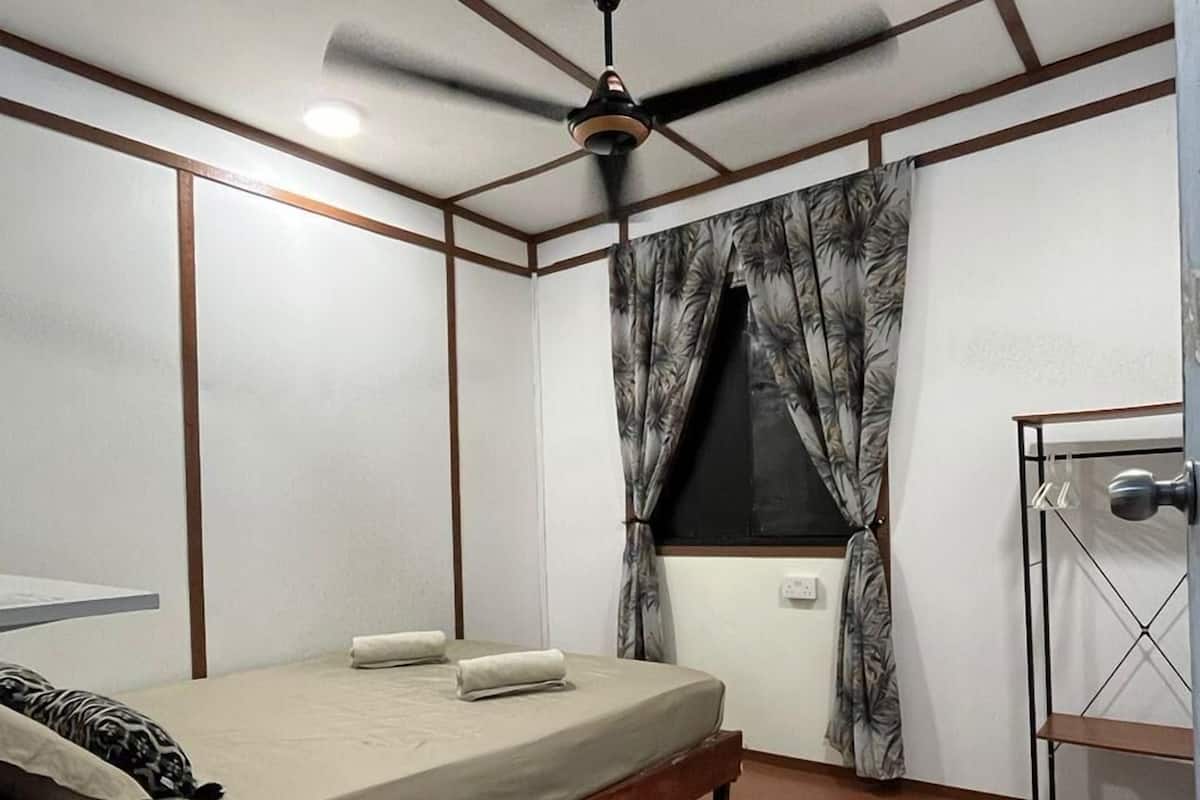 A room with a bed, a ceiling fan, a window with curtains, and a metal rack.