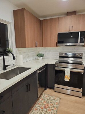 A modern kitchen with wooden cabinets, a built-in microwave, a stainless steel oven, and a black dishwasher. - Peaceful 3-bedroom house in welcoming Seattle neighborhood (Seattle)