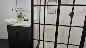Een moderne badkamer met een douchecabine van glas, een vloer van marmer en een zwart wastafelmeubel met een wastafel en handdoek.
