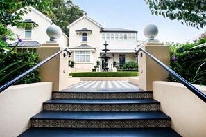 Eine Treppe führt zu einem Haus mit einem Brunnen, umgeben von Grünflächen.