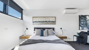 Una camera da letto moderna con un letto grande, due comodini con lampade, un condizionatore d'aria a muro e un grande quadro astratto.