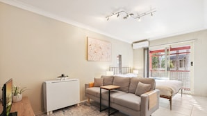 Ein modernes Schlafzimmer mit Schlafsofa, Nachttisch, kleiner Kommode und Fenster mit Balkonblick.