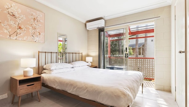 Ein Schlafzimmer mit Bett, Nachttischen, einer Wand-Klimaanlage und einer Glastür, die zu einem Außenbereich führt.