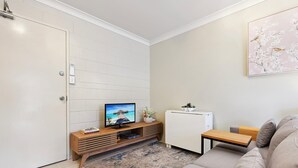 Ein modernes Wohnzimmer mit Fernseher, einem kleinen Tisch, einer Couch und einer Zimmerpflanze.