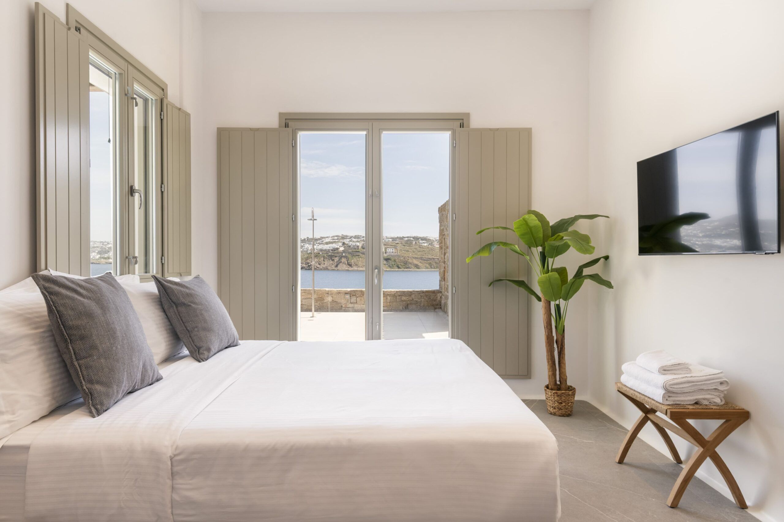 Une chambre avec un lit, une télévision, une plante et une vue sur la mer.