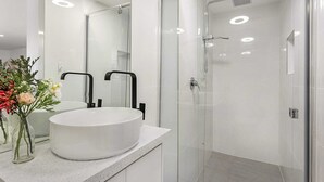 A modern bathroom with a round white sink, a glass shower enclosure, and a mirror above the sink. - Comfy Studio near Racecourse (Carnegie)