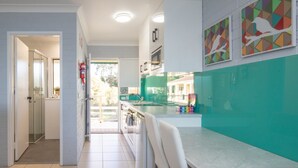 Eine moderne Küche mit grüner Spritzschutzwand, weißen Schränken und einer großen Kochinsel. Zwei Backöfen sind an der Wand montiert, und es gibt einen Kühlschrank.