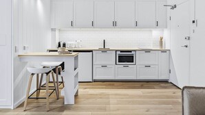 A modern kitchen with white cabinetry, a central island with stools, a built-in oven, and a microwave. - Studio4: Bondi Chic Interiors with Rooftop Pool (Bondi Junction)