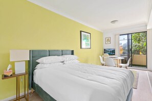 A hotel room with a bed, a bedside table with a lamp, a small table with chairs, and a balcony with a view of greenery. - Serene Studio with Balcony in Prime Location (Wollstonecraft)