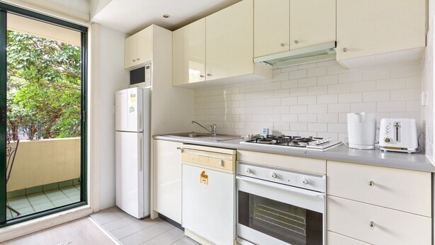 Eine kompakte Küche mit weißen Geräten, einem Geschirrspüler, einem Backofen und einem Gaskochfeld.