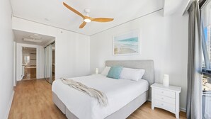 Een slaapkamer met een bed, nachtkastjes, een plafondventilator, een raam met gordijnen en een gang.