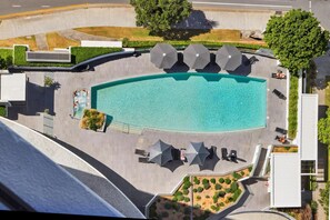 Vista aérea de una piscina con sillas de descanso y sombrillas, rodeada de vegetación y arquitectura moderna.