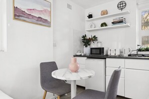 A modern kitchen with white cabinets, a round table with a pink vase, and a gray chair. - Chic Urban Paddington Escape (Paddington)