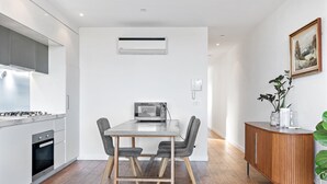 A modern kitchen with a built-in stove, microwave, and a dining area with a table and chairs. - One-Bed Apartment Close to Cafés and Coast (Port Melbourne)