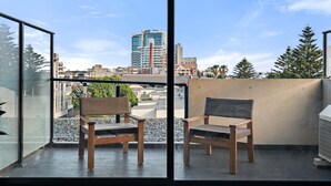 A balcony with two wooden chairs and a glass wall offering a city view. - One-Bed Apartment Close to Cafés and Coast (Port Melbourne)