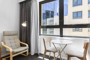 A room with a large window, a grey upholstered chair, a small round table, and a floor lamp.