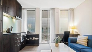 A modern kitchen with dark cabinets, a dining area with a blue sofa, and a sliding glass door leading to a balcony. - Stylish Central Studio with Gym (Melbourne)