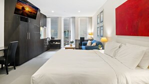 A modern hotel room with a large bed, a desk with a chair, a TV mounted on the wall, and a red accent wall. - Stylish Central Studio with Gym (Melbourne)