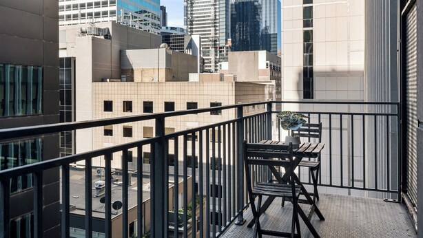 A balcony with a table and chairs, overlooking a cityscape with various buildings. - Stylish Central Studio with Gym (Melbourne)
