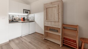 Cozinha compacta com armários brancos, micro-ondas e estante de madeira.