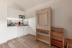 Eine kleine Küche mit weißen Schränken, einer Mikrowelle und einem Holzbodenregal.