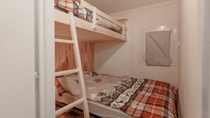 Uma cama beliche com escada, uma janela com cortina e piso de madeira.