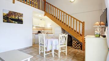 A dining area with a wooden staircase, a table with chairs, a kitchen in the background, and a painting on the wall.