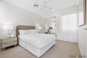 A modern hotel room with a large bed, bedside tables with lamps, a ceiling fan, and a large window with sheer curtains. - Quiet Coastal Retreat with BBQ & Outdoor Space (Hastings Point)
