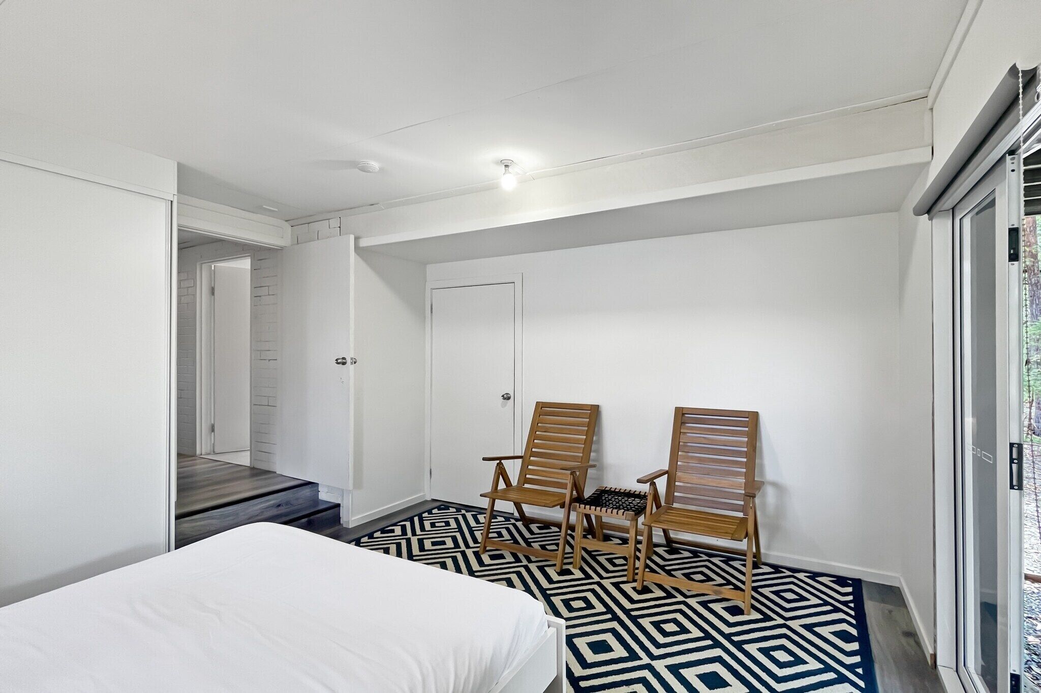 Ein Schlafzimmer mit einem Bett, zwei Holzstühlen, einem gemusterten Teppich und einer Tür zu einer Treppe.