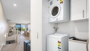 A modern laundry room with a front-loading washer and dryer, a sink, and a staircase leading to an upper level. - Silverwater Stay Near Parks and Cafés (Silverwater)