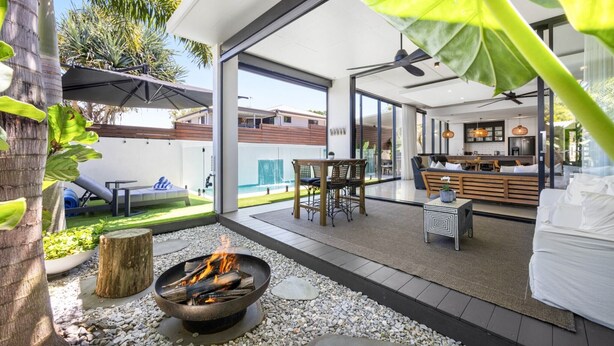 A modern outdoor living area with a fire pit, seating, and a view of the pool. - Spacious 3-Bedroom Retreat with BBQ and Pool (Coolum Beach)