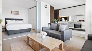 A modern, well-lit bedroom with a large bed, a gray sofa, and a wooden coffee table. - Luxury 2-Bed Apartment in Melbourne's Heart (Melbourne)