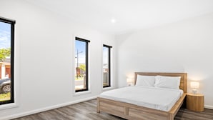 A bedroom with a wooden bed, two windows, a nightstand, and a view of the outside.