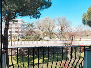 A balcony with a metal railing overlooking a landscaped area with trees and a building in the background. - Spacious apartment in Cavallino (Lido di Jesolo)
