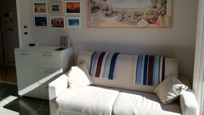 A living room with a sofa, a white cabinet, and a wall with framed pictures. - La Dolce Vita, a stone's throw from the beach. (rimini)