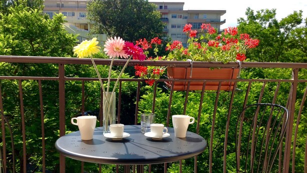 A balcony with a round table and two chairs, a potted plant with flowers, and a railing. - La Dolce Vita, a stone's throw from the beach. (rimini)