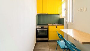 Una cocina compacta con gabinetes amarillos, un horno de acero inoxidable, un lavamanos y una silla azul.
