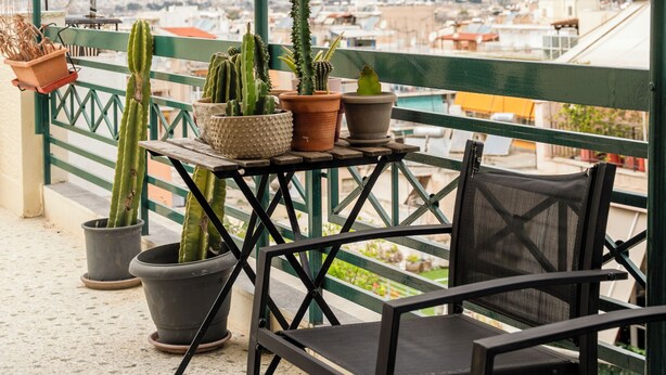 Un balcón con cactus en macetas, una mesa y sillas, con vistas a un paisaje urbano.