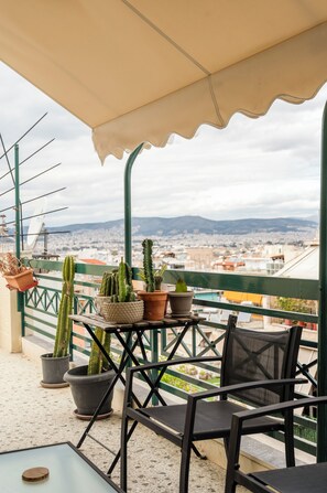 A balcony with potted cacti, a table, and chairs, overlooking a cityscape. - Cozy 1-bedroom apartment with a big terrace near center of Athens with AC (Athina)