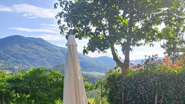 Een terras met een tafel en stoelen, een grote parasol en een uitzicht op bergen.