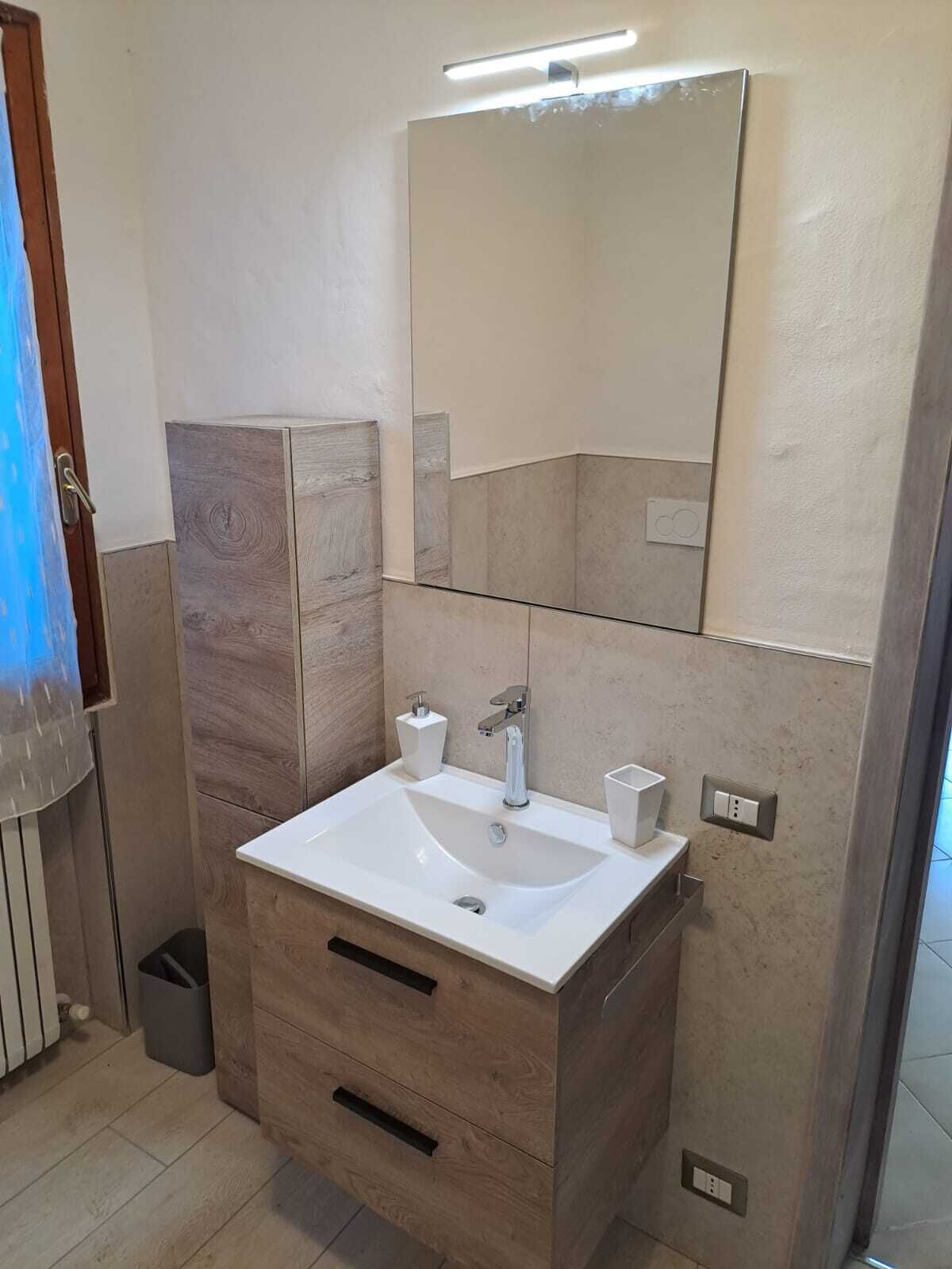 A modern bathroom with a white sink, wooden vanity, and a large mirror.